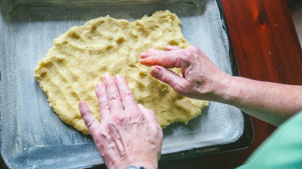 Těsto na plech namačkáme a roztlačíme rukama. Chce to trpělivost | foto: Jana Volková Těsto na plech namačkáme a roztlačíme rukama. Chce to trpělivost